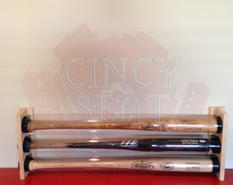 May include: Three baseball bats are displayed in a wooden rack with clear protective tubes. The bats are all different brands and have different signatures on them.