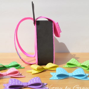 Puede incluir: Una bolsa de artesan&iacute;a de espuma rosa con un asa de espuma negra y lunares blancos. La bolsa est&aacute; sentada sobre una superficie de madera con varios lazos de espuma de colores con lunares blancos.