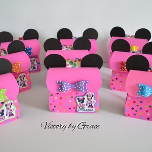 Puede incluir: Cajas de regalo de fiesta de Minnie Mouse en rosa y negro con patrones de lunares, lazos e im&aacute;genes de personajes de Minnie Mouse. Las cajas est&aacute;n decoradas con el n&uacute;mero "2" y el nombre "Mileena".