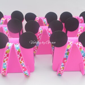 Puede incluir: Cajas de regalo de fiesta rosas con orejas de Mickey Mouse negras y cinta de lunares de colores. Las cajas est&aacute;n decoradas con el texto "Victory by Grace".