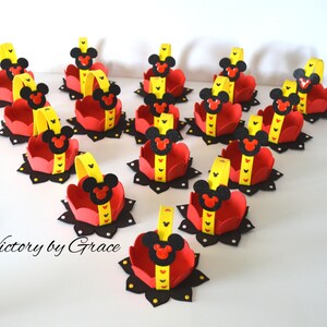 May include: A set of 15 small red and yellow felt baskets with black Mickey Mouse ears and faces. The baskets have yellow handles and black polka dots. The text "Victory by Grace" is visible in the bottom left corner of the image.