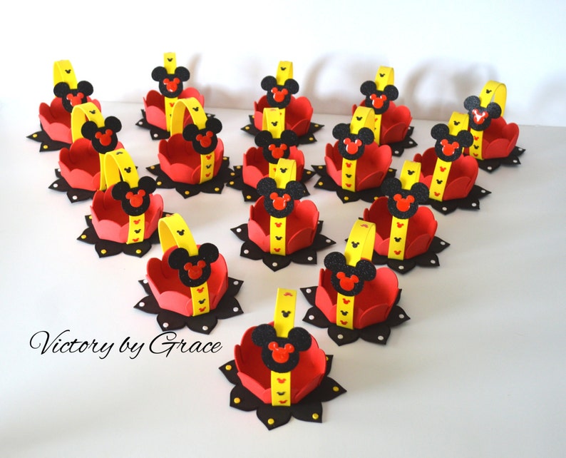 May include: A set of 15 small red and yellow felt baskets with black Mickey Mouse ears and faces. The baskets have yellow handles and black polka dots. The text "Victory by Grace" is visible in the bottom left corner of the image.