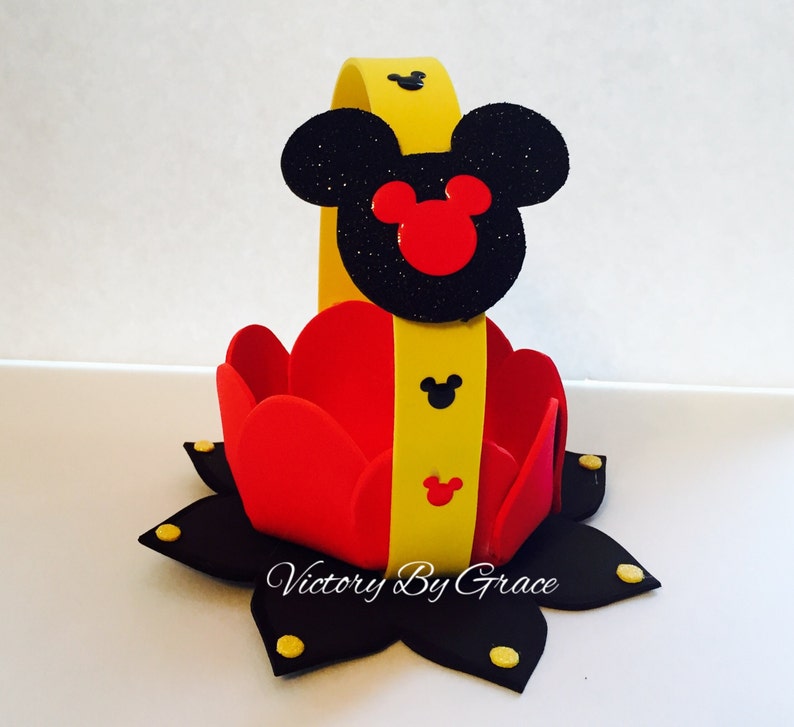 May include: A red and yellow Mickey Mouse themed party favor basket. The basket is made of foam and has a yellow handle with a black Mickey Mouse head on top. The basket is decorated with black and yellow polka dots.