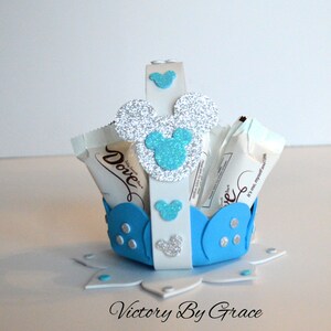 May include: A blue and white Mickey Mouse themed favor basket with a silver glitter Mickey Mouse head on the front. The basket is filled with Dove chocolate bars. The basket is sitting on a white surface with the words "Victory By Grace" written on it.