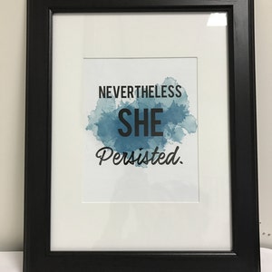 以下が含まれることがあります： 青い水彩画の背景と「Nevertheless she persisted.」というテキストが書かれた額装されたプリント