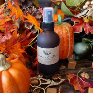 May include: A dark brown spray bottle with a label reading "Potatoes & Molasses" is surrounded by fall foliage, pumpkins, and candies. The bottle contains 4 fl oz (118 mL) of room and linen spray.
