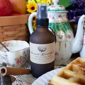 May include: A brown glass bottle with a black spray nozzle and a label that reads "Second Breakfast Room and Linen Spray Pumpkin | Vanilla | Cinnamon | Pecan 4 oz | 118 ml".