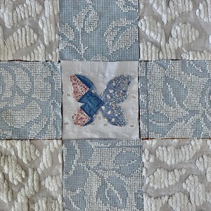 May include: A patchwork design featuring nine squares with varying textures and patterns. The squares are primarily in shades of white and blue. A central square showcases a butterfly applique with floral and denim fabrics. The overall aesthetic is reminiscent of a handcrafted quilt.