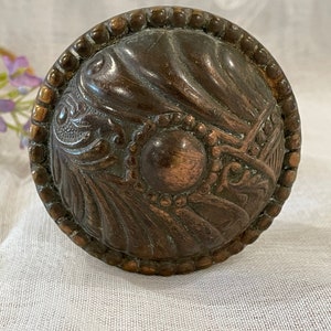 May include: A vintage, ornate, brass door knob with a detailed, swirling design. The knob has a raised, circular center and a beaded outer edge.