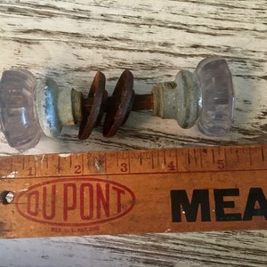 May include: A pair of antique glass door knobs with a rusty metal spindle. The knobs are a pale lavender color and have a faceted design. The spindle is approximately 3 inches long.