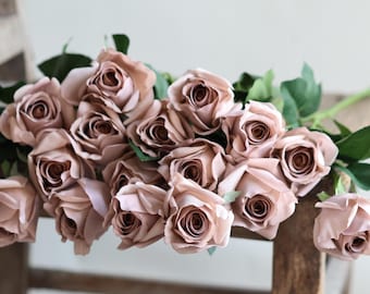 May include: A bouquet of dusty rose silk roses arranged on a wooden chair. The roses are arranged in a loose, natural style, with some of the roses overlapping each other.