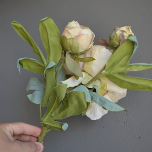 May include: A bouquet of artificial peonies with pale pink and white petals and green leaves.