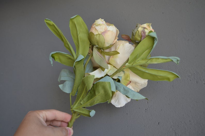 May include: A bouquet of artificial peonies with pale pink and white petals and green leaves.