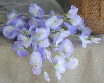 May include: A bouquet of purple and white artificial sweet pea flowers. The flowers are arranged in a cluster and have a delicate, feminine appearance.