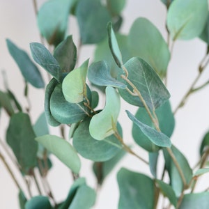 Op de afbeelding: Een close-up van een bos kunstmatige eucalyptusbladeren. De bladeren zijn lichtgroen van kleur en hebben een zachte, fluweelachtige textuur.