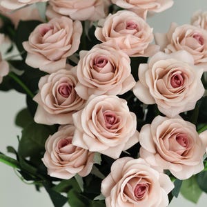 Puede incluir: Un ramo de rosas artificiales de color rosa claro con hojas verdes.