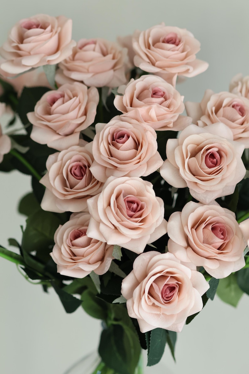 Puede incluir: Un ramo de rosas artificiales de color rosa claro con hojas verdes.