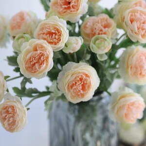 Puede incluir: Un ramo de flores artificiales de color melocot&oacute;n en un jarr&oacute;n. Las flores tienen una textura delicada y rizada y est&aacute;n dispuestas en un estilo suelto y natural.