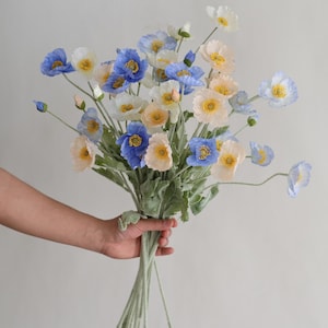 Puede incluir: Un ramo de flores artificiales de amapola azul, blanco y melocot&oacute;n con tallos verdes.