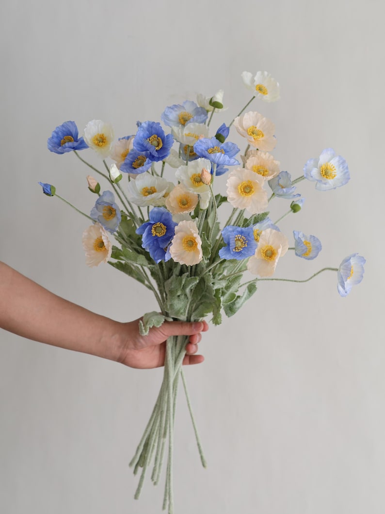 Puede incluir: Un ramo de flores artificiales de amapola azul, blanco y melocot&oacute;n con tallos verdes.