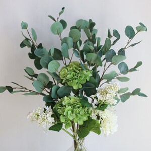 Op de afbeelding: Een boeket kunstbloemen met groene hortensia's en witte bloemen, gearrangeerd met eucalyptus takken.