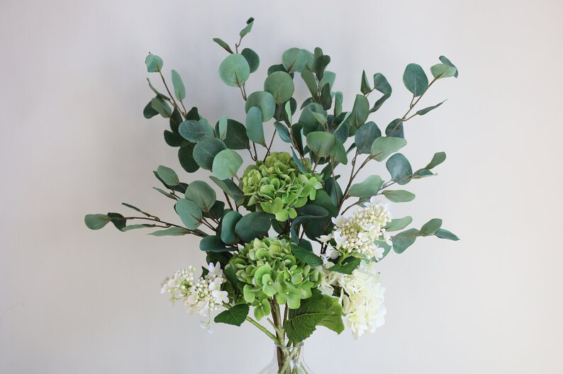 Op de afbeelding: Een boeket kunstbloemen met groene hortensia's en witte bloemen, gearrangeerd met eucalyptus takken.