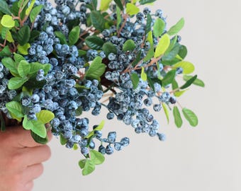 May include: A bouquet of artificial blue berry sprigs with green leaves.