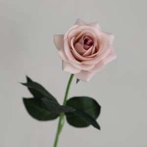 Puede incluir: Una sola rosa artificial de color rosa claro con un centro rosa m&aacute;s oscuro. La rosa tiene hojas verdes y un tallo largo.