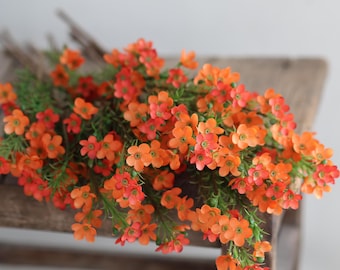 May include: A bunch of artificial orange flowers with green stems. The flowers are small and delicate, and they are arranged in a loose, flowing bouquet.