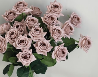 May include: A bouquet of dusty rose artificial roses with green leaves in a clear glass vase.