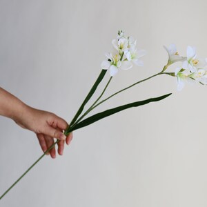 May include: A bouquet of white artificial freesia flowers with green stems and leaves.