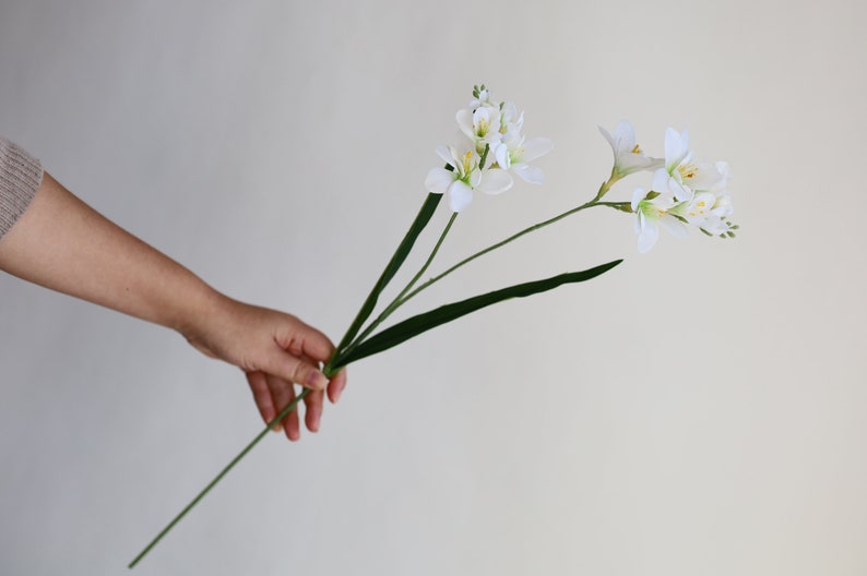 May include: A bouquet of white artificial freesia flowers with green stems and leaves.