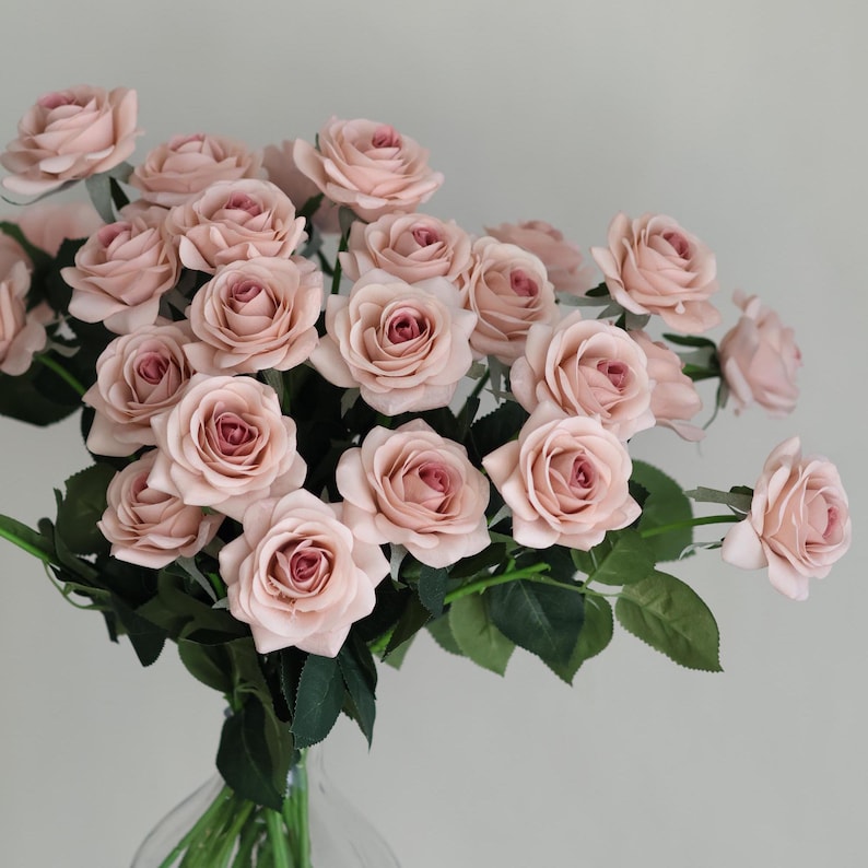 Puede incluir: Un ramo de rosas artificiales de color rosa claro con tallos y hojas verdes.