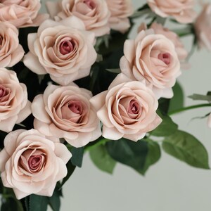 Puede incluir: Un ramo de rosas artificiales de color rosa claro con tallos y hojas verdes.