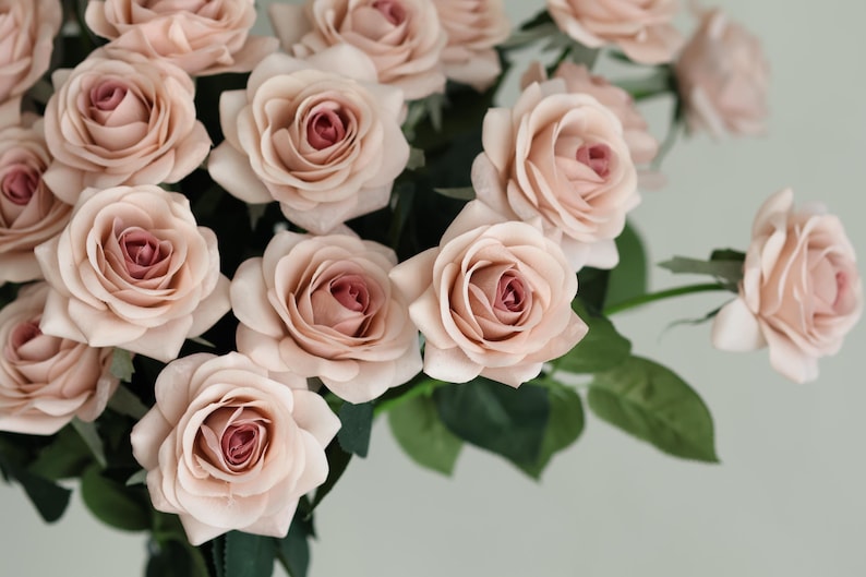 Puede incluir: Un ramo de rosas artificiales de color rosa claro con tallos y hojas verdes.