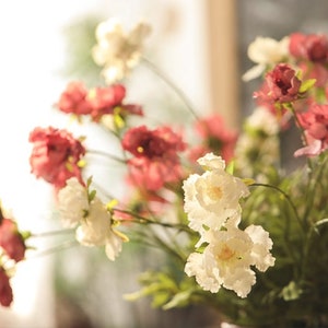 May include: A bouquet of artificial flowers featuring a mix of deep red and creamy white blossoms. The flowers have layered, ruffled petals and are attached to thin green stems with small green leaves, creating a dense, multi-layered floral arrangement.