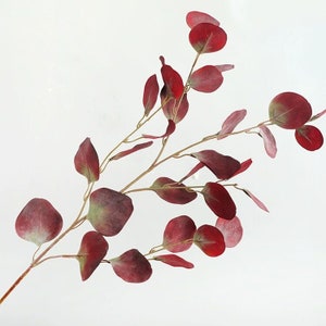 May include: A sprig of artificial eucalyptus with burgundy leaves. The leaves are arranged in a natural, flowing pattern.