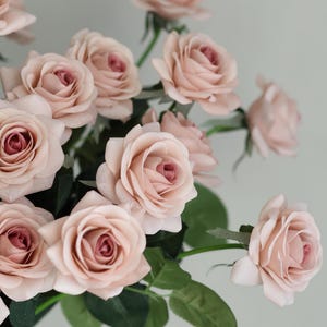 Puede incluir: Un ramo de rosas artificiales de color rosa claro con hojas verdes. Las rosas est&aacute;n dispuestas en un racimo, con algunos tallos visibles.