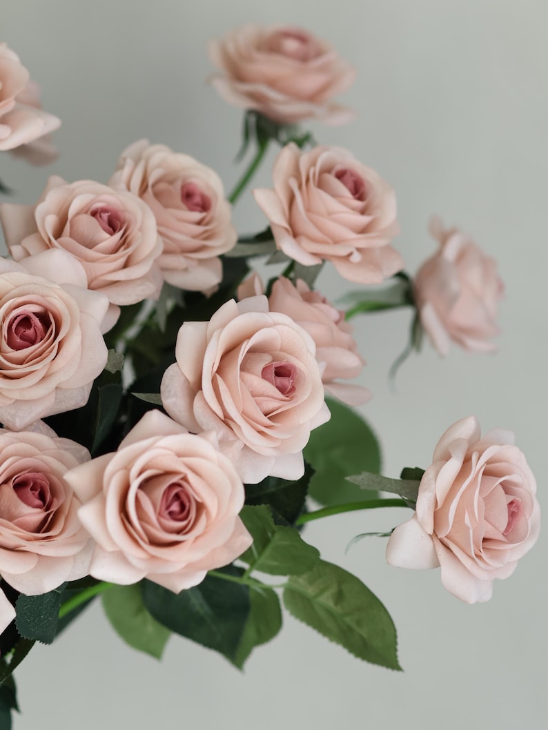 Puede incluir: Un ramo de rosas artificiales de color rosa claro con hojas verdes. Las rosas est&aacute;n dispuestas en un racimo, con algunos tallos visibles.