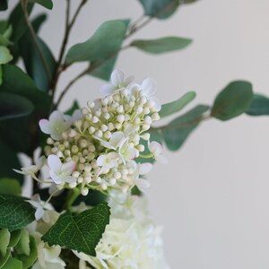 Op de afbeelding: Een boeket witte en groene bloemen met kleine witte bloesems en groene bladeren.
