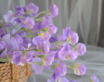 May include: A bouquet of purple sweet pea flowers arranged in a woven basket. The flowers are delicate and have a soft, pastel color.