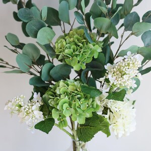 Op de afbeelding: Een boeket kunstbloemen met groene hortensia's en witte bloemen, gearrangeerd met eucalyptusbladeren.