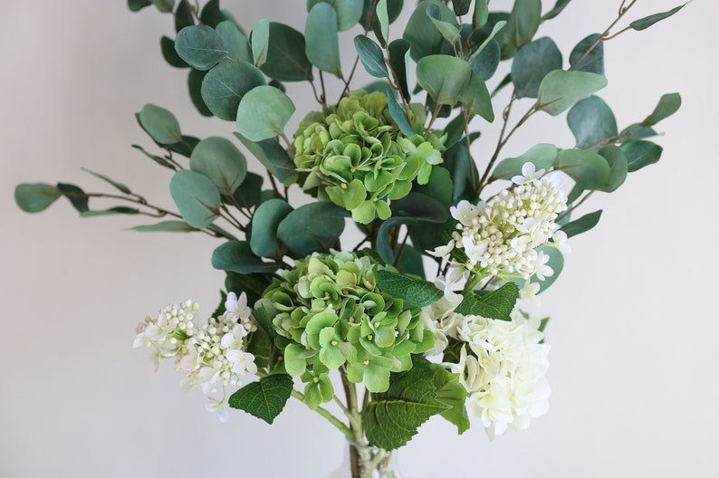 Op de afbeelding: Een boeket kunstbloemen met groene hortensia's en witte bloemen, gearrangeerd met eucalyptusbladeren.