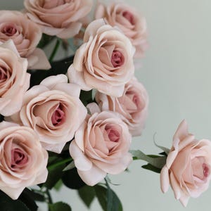 Puede incluir: Un ramo de rosas artificiales de color rosa claro con tallos y hojas verdes.