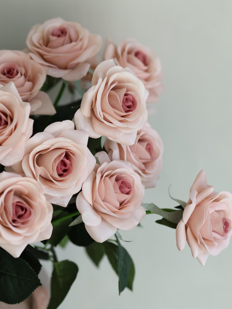 Puede incluir: Un ramo de rosas artificiales de color rosa claro con tallos y hojas verdes.