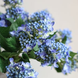 May include: A bouquet of blue artificial hydrangea flowers with green leaves.