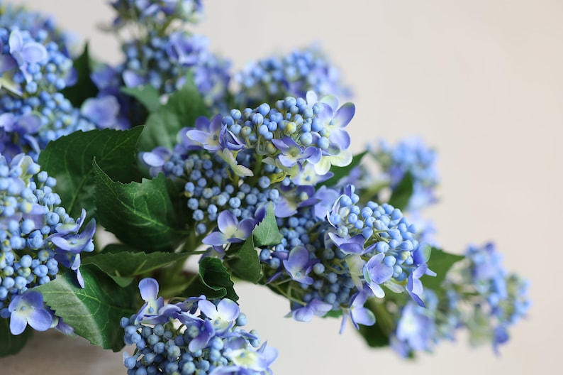 May include: A bouquet of blue artificial hydrangea flowers with green leaves.