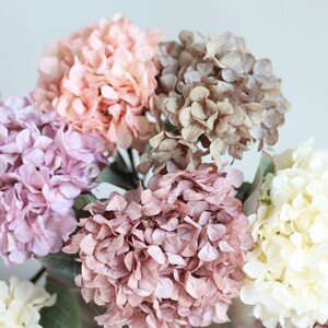 Puede incluir: Un ramo de flores de hortensia artificiales en varios tonos de rosa, morado y blanco. Las flores est&aacute;n dispuestas en un racimo, con los tallos ocultos a la vista.