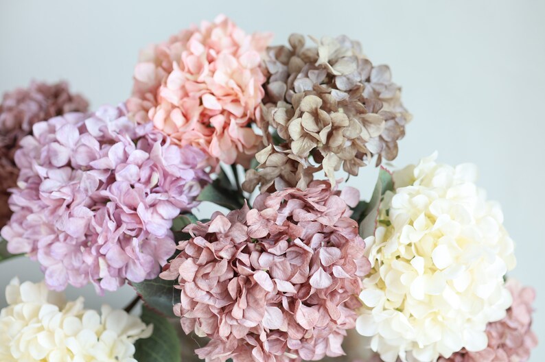 Puede incluir: Un ramo de flores de hortensia artificiales en varios tonos de rosa, morado y blanco. Las flores est&aacute;n dispuestas en un racimo, con los tallos ocultos a la vista.
