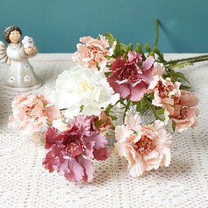 Op de afbeelding: Een boeket kunstbloemen in tinten roze, wit en bordeauxrood. De bloemen hebben een delicate, gekrulde textuur en zijn in een vaas gerangschikt.